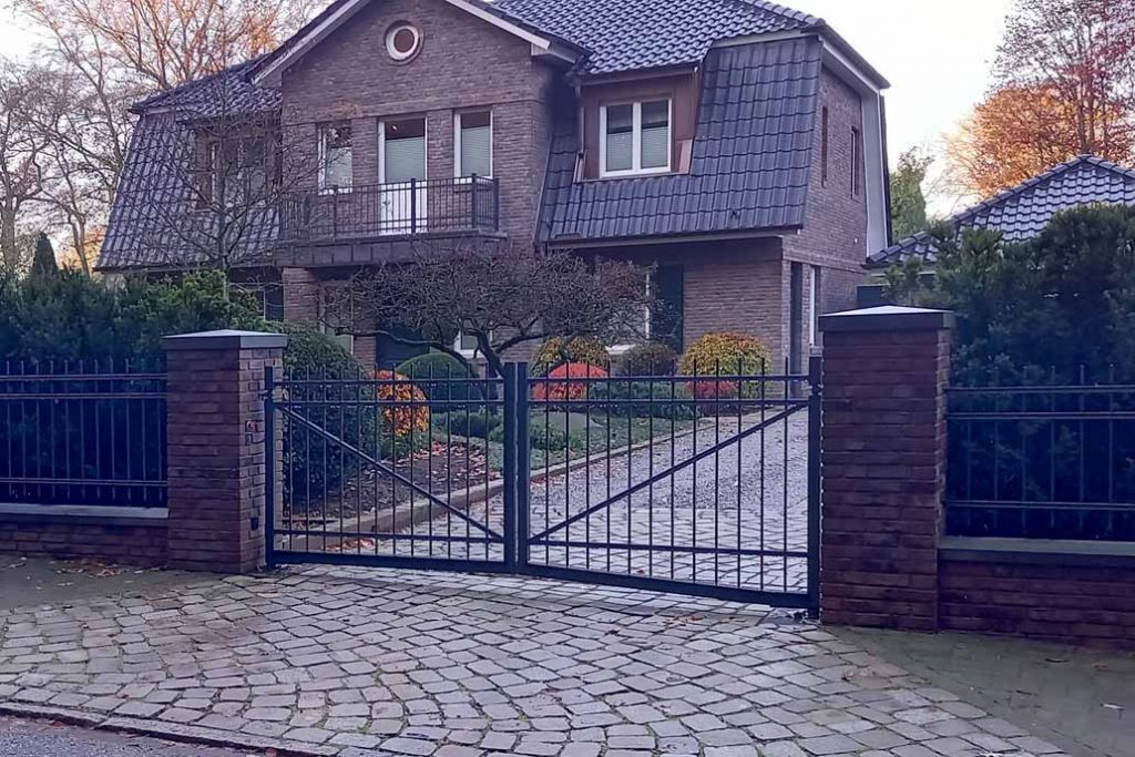 Drehflügeltor zwischen roten Mauerpfosten an einer Villa aus rotem Klinker .