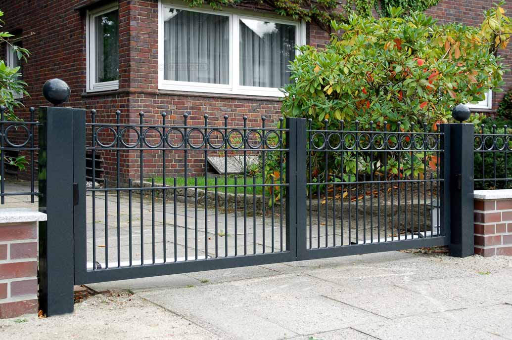 Drehflügeltor im Hanseatenstil mit Ringen in der Torfüllung und Kugeln als Stababschluß vor einem Rotklinkerhaus.
