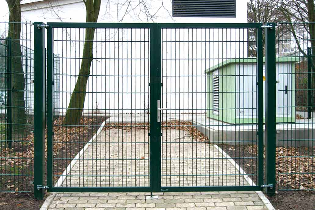 Grünes zwei Meter hohes Drehflügeltor mit Stahlmattenfüllung vor einem Gewerbebau.