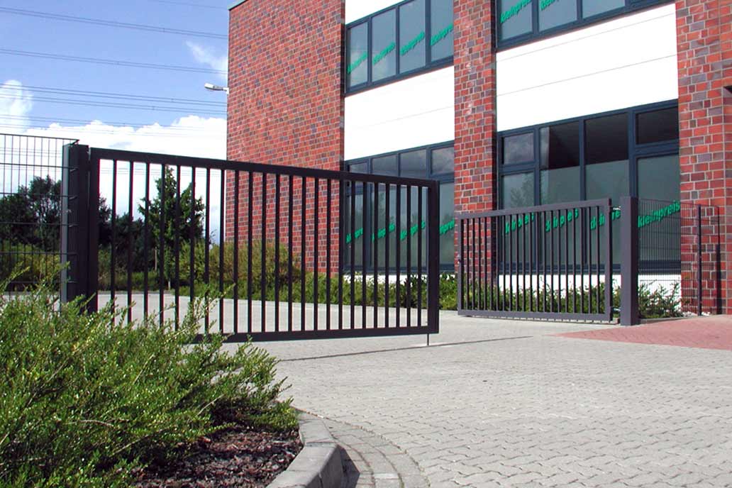 Anthrazit beschichtetes Drehflügeltor mit Stabfüllung vor einem Gewerbebau.