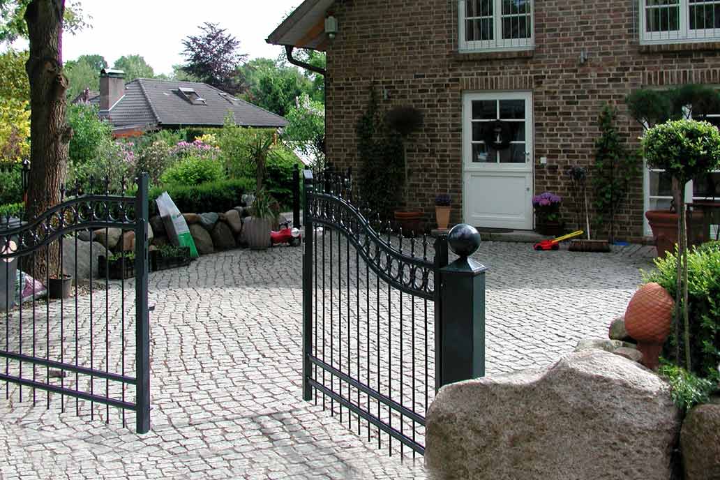 Geschwungenes Drehflügeltor im Hanseatenstil mit Pfeilspitzen und Ringen vor einem Einfamilienhaus.