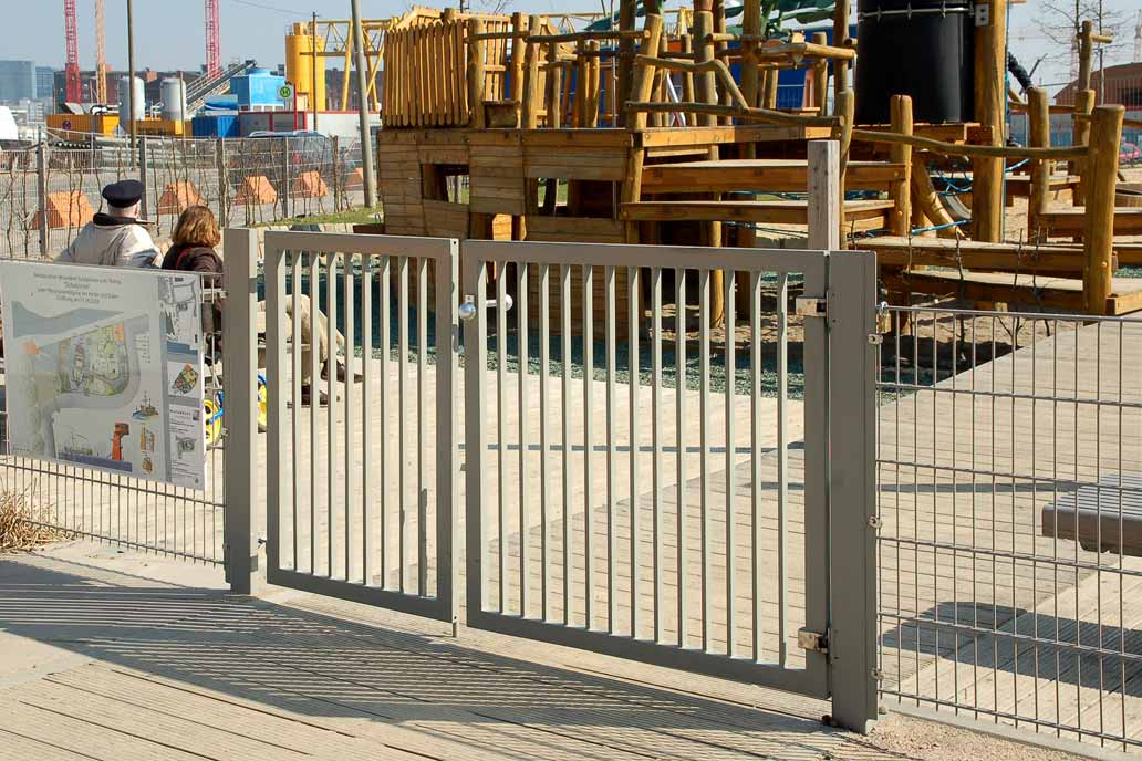 Hellgrau beschichtetes Schwingflügeltor am Zugang zu einem Spielplatz in der Hafencity Hamburg.