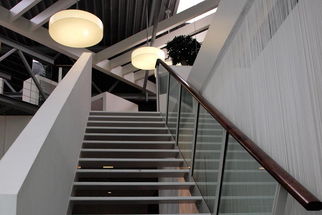Eine Stahltreppe mit einem Glasgeländer und Holzhandlauf.